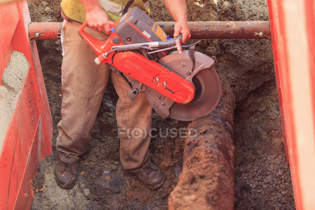 Construction worker using saw to cut through old water pipe — Stock Photo