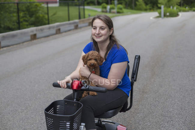 Mujer joven con parálisis cerebral montando el scooter con su perro - foto de stock