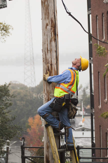 Cable lineman subiendo una escalera en el poste de poder de la ciudad - foto de stock