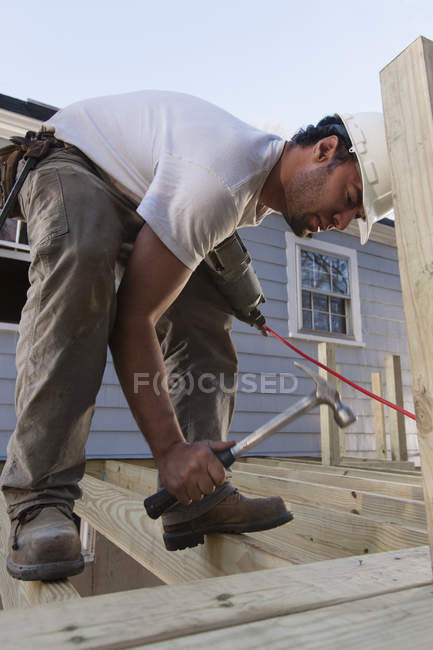 Carpintero hispano parado en vigas de cubierta para clavar clavos en la — Lugar de construcción, MALO - Stock | #317474444