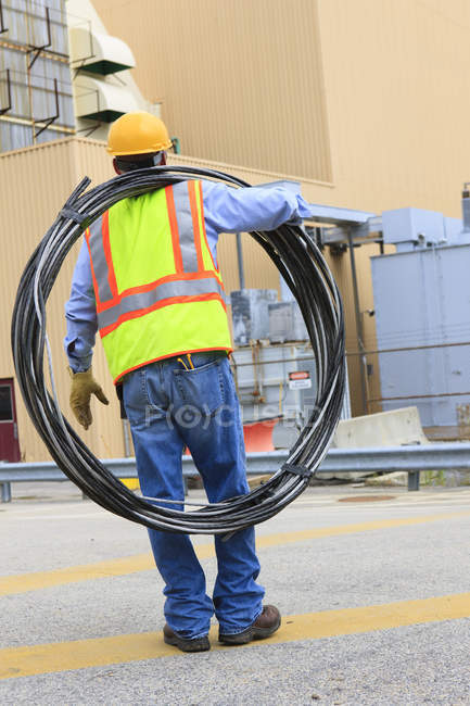 Engineer at electric power plant carrying coil of wire at storage area — Stock Photo