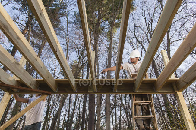 Hispanic carpenter installing first decking with corner cuts around deck posts — Stock Photo