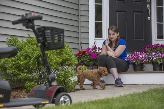 Молодая женщина с церебральным параличом играет со своей собакой, пока её скутер там — стоковое фото