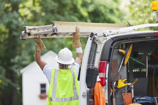Communications worker loading a ladder onto a truck — Stock Photo