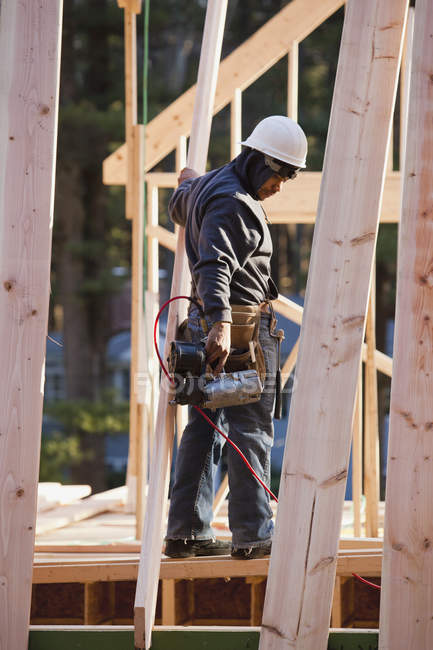 Carpenter with a nail gun working on rafters — Stock Photo