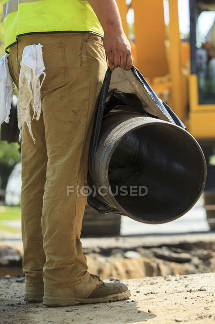 Construction worker holding water main pipe suspended by excavator — Stock Photo
