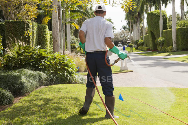 Pest control technician using high pressure spray gun and hose on  lawns — Stock Photo