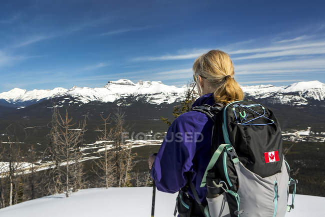 Female hiker on snow-covered pathway with mountains, blue sky and clouds in the background; Lake Louise, Alberta, Canada — Stock Photo