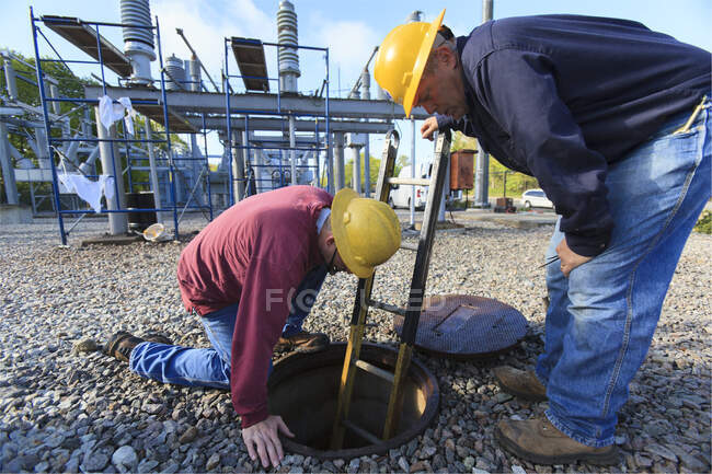 Power engineers placing ladder inside manhole at high voltage power distribution station — Stock Photo