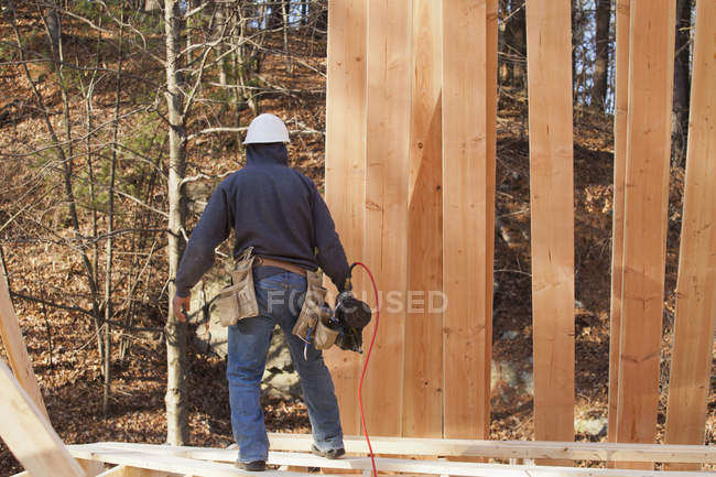 Carpinteiro com uma pistola de pregos em uma casa em construção — Fotografia de Stock