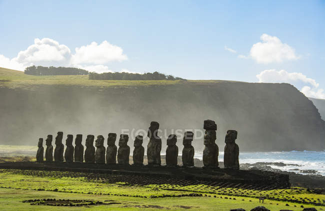 The fifteen moais of Tongariki seen from afar in decreasing perspective against the ocean and blue sky; Easter Island, Chile — Stock Photo