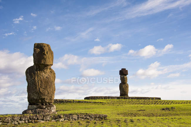 A grassy slope leads the eye towards two moais, seen against an early morning blue sky, Easter Island, Chile — стокове фото