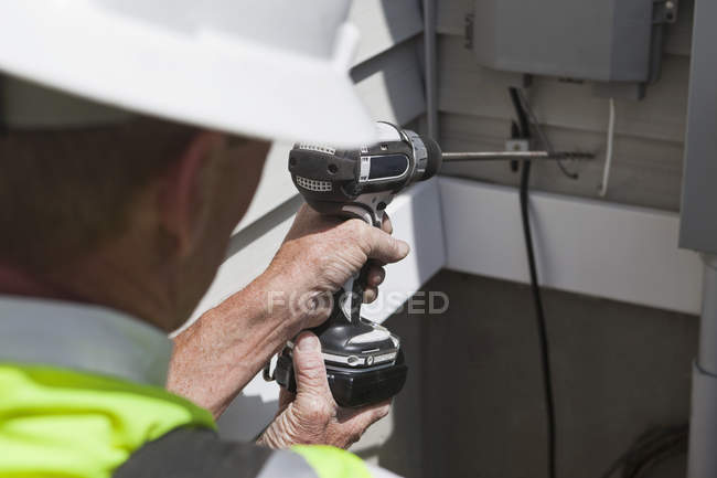 Communications worker drilling access hole through exterior wall — Stock Photo