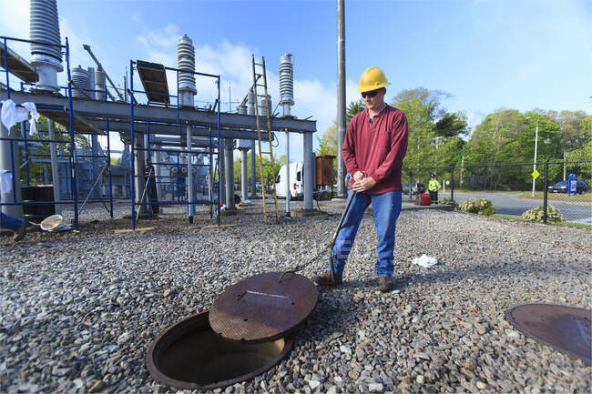 Power engineer accessing manhole cover at high voltage power distribution station, — Stock Photo