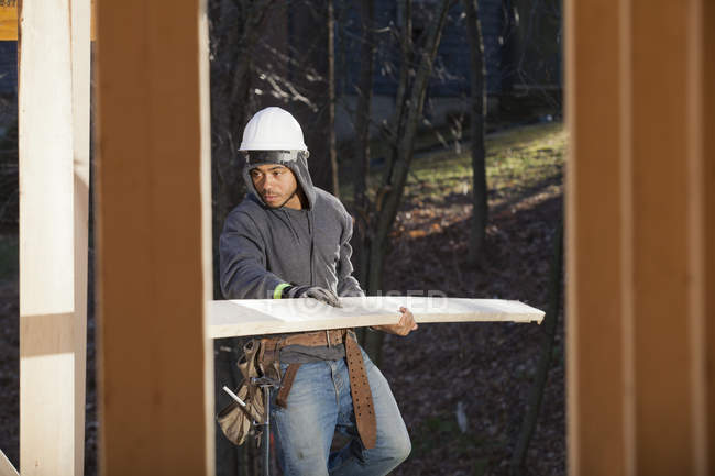 Carpintero llevando una tabla para la construcción de casas - foto de stock