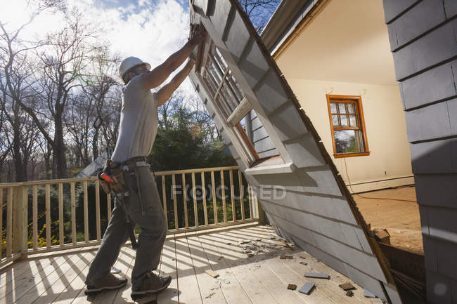 Carpintero hispano eliminando el recién cortado acceso a la cubierta en casa - foto de stock