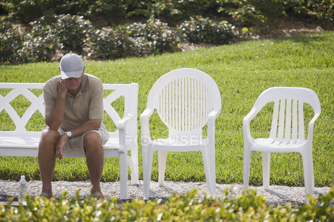 Uomo anziano seduto su una panchina con la mano sul mento — Foto stock