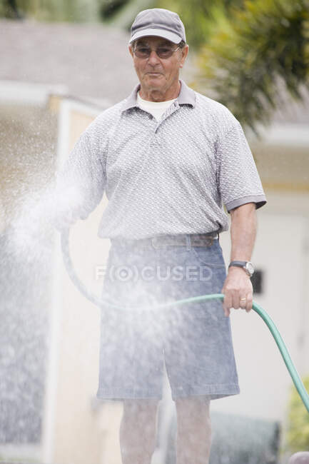 Homem sênior pulverizando água com uma mangueira — Fotografia de Stock