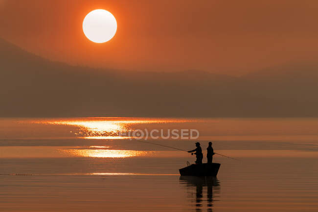 Силуетанги стоять на човні й ловлять лосося на заході сонця; Джуно, Аляска, Сполучені Штати Америки. — стокове фото