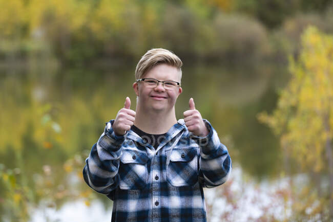 Молодий чоловік з синдромом Дауна, який теплим осіннім вечором простягає великий палець до міського парку: Едмонтон, Альберта, Канада. — стокове фото