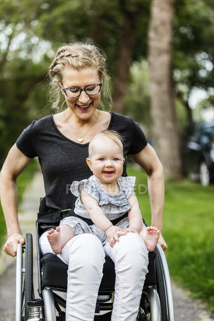 A paraplegic mom carrying her baby in her lap while using a wheelchair outdoors on a warm summer afternoon: Edmonton, Alberta, Canada — Stock Photo