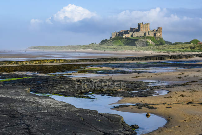 Bamburgh Castle with the tide out showing rocky coastline; Bamburgh, Northumberland, England — Stock Photo