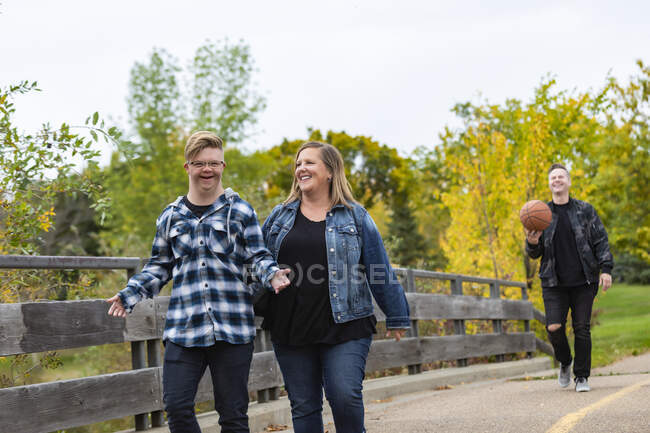 A young man with Down Syndrome walking with his father and mother while enjoying each other's company in a city park on a warm fall evening: Edmonton, Alberta, Canada — Stock Photo