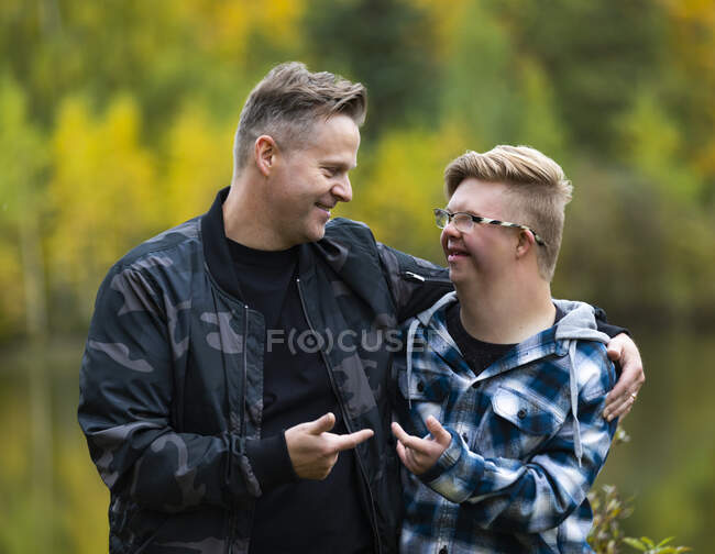 A young man with Down Syndrome and his father enjoying each other's company and giving each other funny hand gestures in a city park on a warm fall evening: Edmonton, Alberta, Canada — Stock Photo