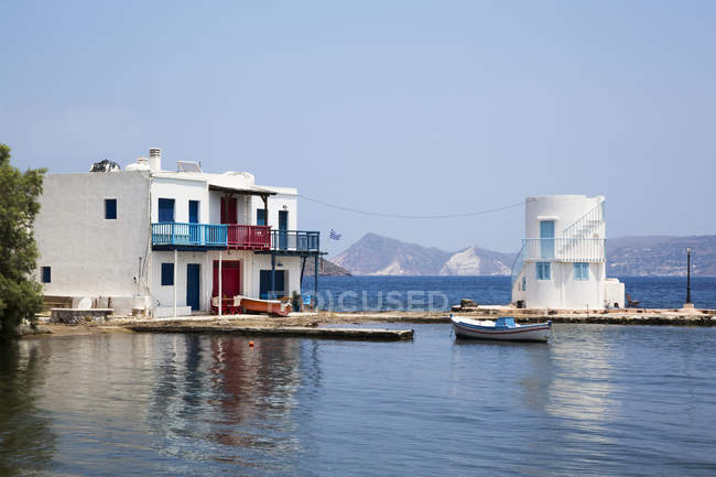 Embourios village with a residential building on the water's edge and a small boat moored off the dock; Embourios, Milos Island, Cyclades, Greece — Stock Photo
