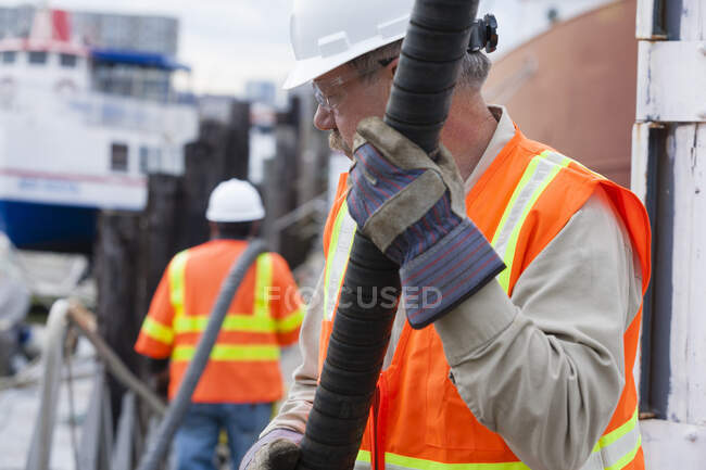 Environmental engineer extending petroleum hose for toxic waste cleanup to commercial ship — Stock Photo