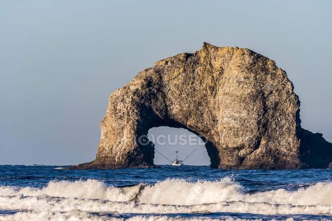 Un barco pesquero está enmarcado por un arco de piedra en Rockaway Beach; Rockaway, Oregon, Estados Unidos de América - foto de stock