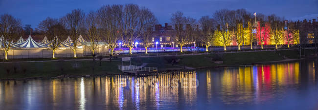 Hampton Court mit Weihnachtsbeleuchtung, die leuchtet und sich im Wasser spiegelt; London, England — Stockfoto