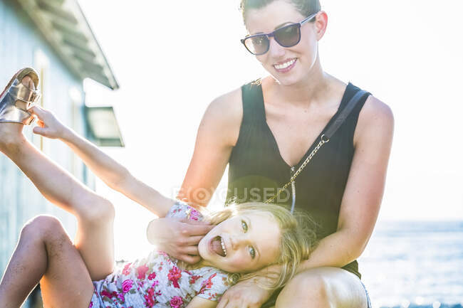 Retrato de una madre y su hija sentadas juntas mientras estaban de vacaciones en Lahaina a lo largo de Front Street bajo la luz del sol brillante con el Océano Pacífico en el fondo; Lahaina, Maui, Hawaii, Estados Unidos de América - foto de stock