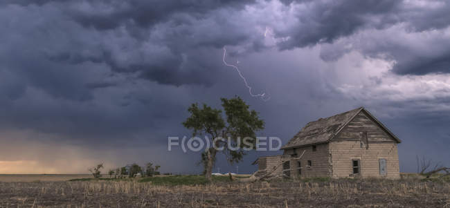 A forked lightning bolt descends from a weak thunderstorm near an abandoned building; Guymon, Oklahoma, United States of America — Stock Photo