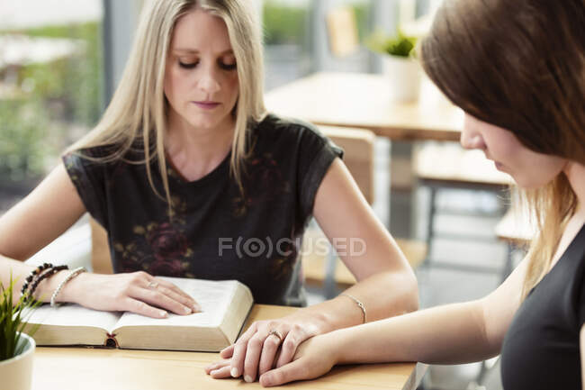 A mature Christian woman mentoring and praying with a young woman during a bible study in a coffee shop at a church: Edmonton, Alberta, Canada — Stock Photo