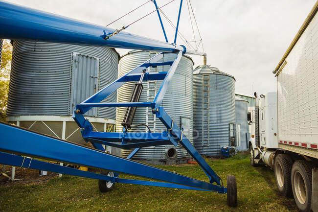 Eine Schneckenmontage und ein Getreidewagen, die neben Silos auf einem Hof abgestellt sind; Legal, Alberta, Kanada — Stockfoto