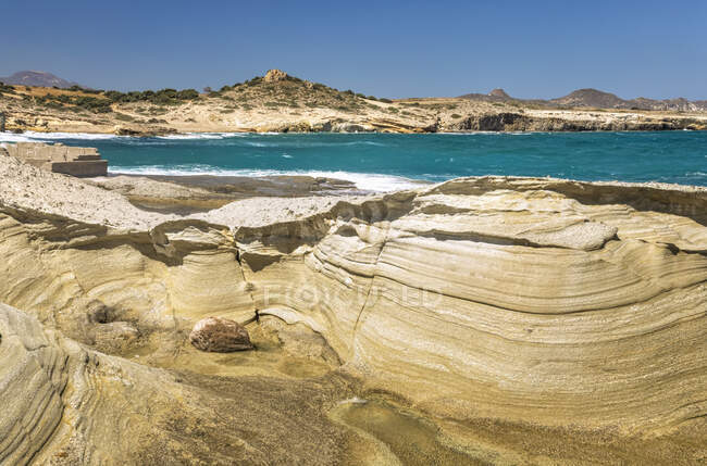 Эродированные скальные образования вдоль берега и бирюзовые воды океана вдоль побережья греческого острова; Милош, Греция — стоковое фото