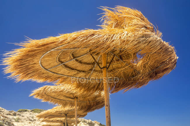 Thatch beach structures blowing in the wind and a bright blue sky; Milos, Greece — Foto stock