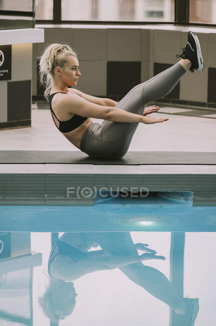 Mulher trabalhando em um tapete fazendo um exercício abdominal ao lado de uma piscina; Wellington, Nova Zelândia — Fotografia de Stock