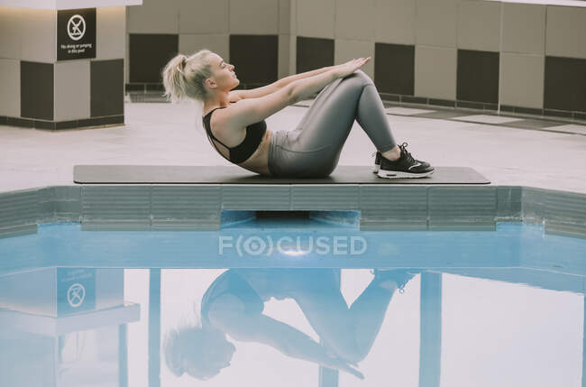 Woman working out on a mat doing an abdominal exercise beside a pool; Wellington, New Zealand — Stock Photo