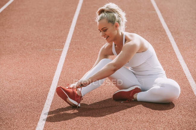 Mujer atándose el cordón de los zapatos para prepararse para correr en una pista; Wellington, Nueva Zelanda - foto de stock