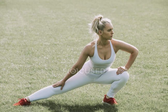 Woman stretching her leg muscles on a grass field; Wellington, New Zealand — Stock Photo