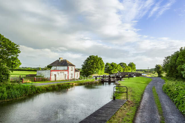 Altes rot-weißes Haus neben einer Schleuse am großen Kanal in Kildare an einem Sommerabend; Rathangan, County Kildare, Irland — Stockfoto