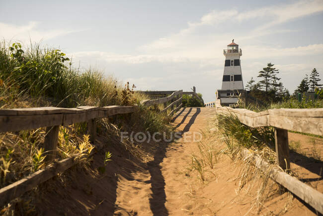 Sentiero sabbioso e recinzione in legno che conduce ad un faro sulla costa; Isola del Principe Edoardo, Canada — Foto stock