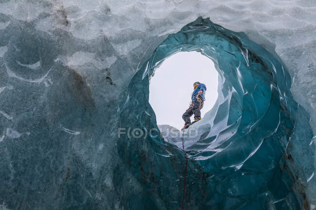 Hombre explorando una cueva de hielo; Costa Sur, Islandia - foto de stock
