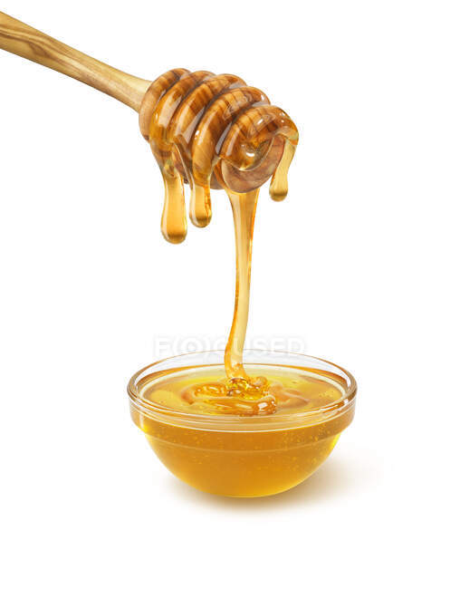 Vue rapprochée de la trempette couverte de miel goutte à goutte dans un bol de miel sur fond blanc — Photo de stock