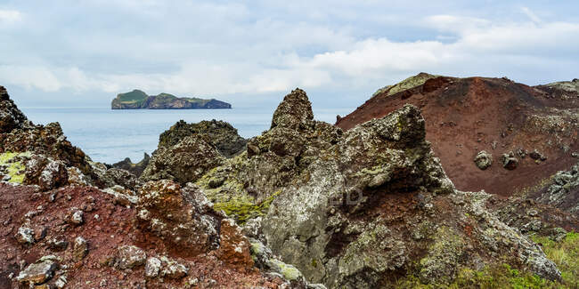 Rocher accidenté le long de la côte de l'île de Heimaey, avec vue sur l'île d'Ellioaey, une partie d'un archipel le long de la côte sud de l'Islande ; Vestmannaeyjar, région sud, Islande — Photo de stock