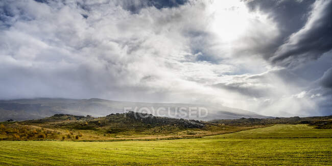 Campo verde y luz solar filtrándose a través de las nubes en Islandia Oriental; Fljotsdalsherao, Región Oriental, Islandia - foto de stock