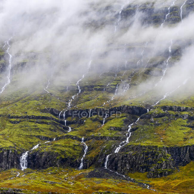 Cascate che scorrono su un fianco della montagna; Djupivogur, Regione orientale, Islanda — Foto stock