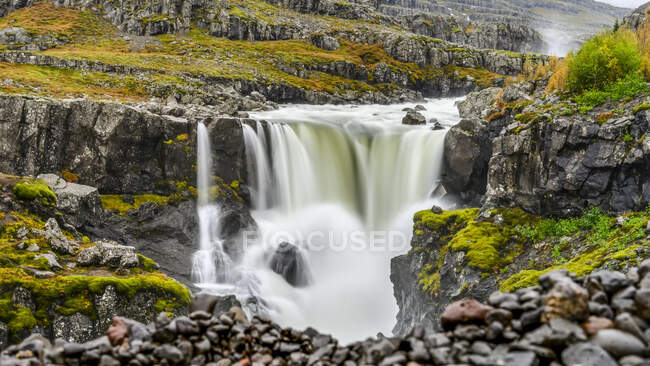Ein Wasserfall über einer felsigen Landschaft in herbstlichen Farben; Djupivogur, östliche Region, Island — Stockfoto